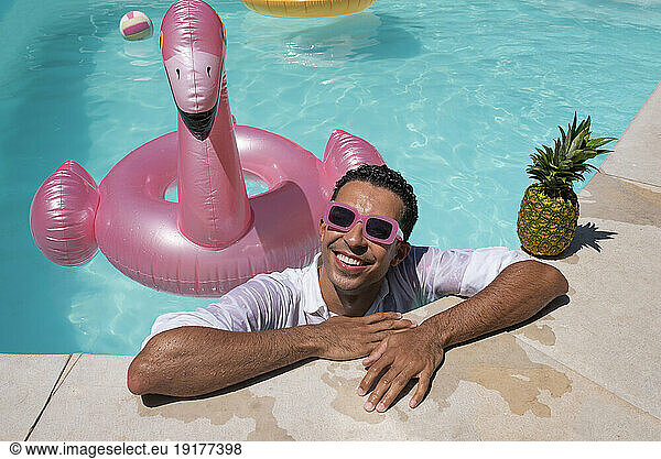 Happy man leaning with pineapple and inflatable swimming ring by poolside