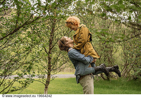 Happy man lifting girlfriend in park on sunny day