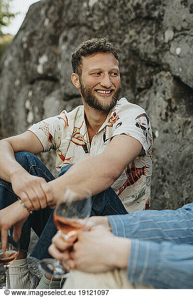 Happy man looking away while having wine with friend