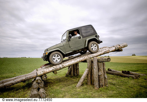 Happy man parking jeep on wooden logs at field