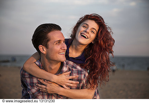 Happy man piggybacking woman at beach during sunset