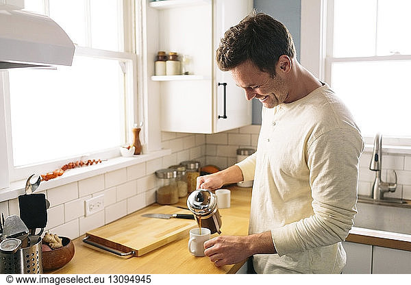 Happy man pouring coffee while standing by kitchen counter at home