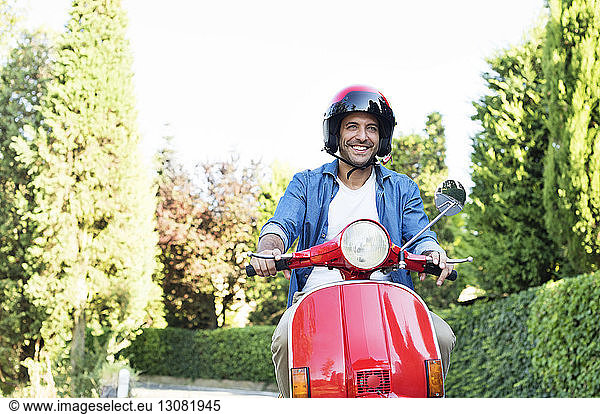 Happy man riding motor scooter amidst trees