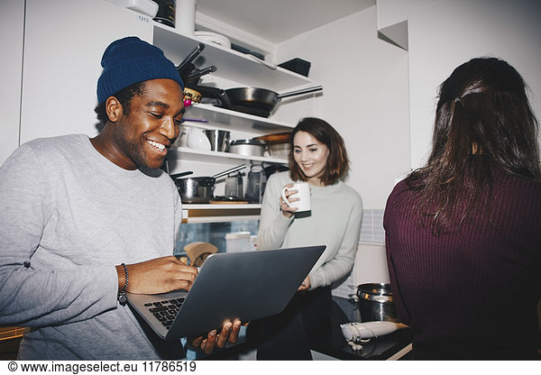 Happy man showing laptop to female friend with coffee cup in kitchen