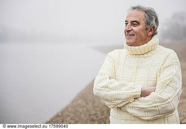 Happy man standing with arms crossed at beach