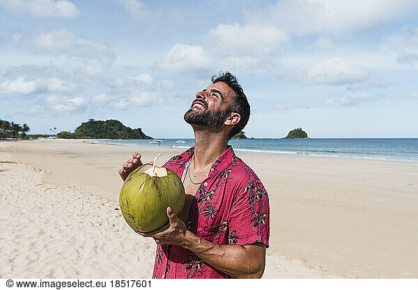 Happy man standing with coconut water enjoying at beach