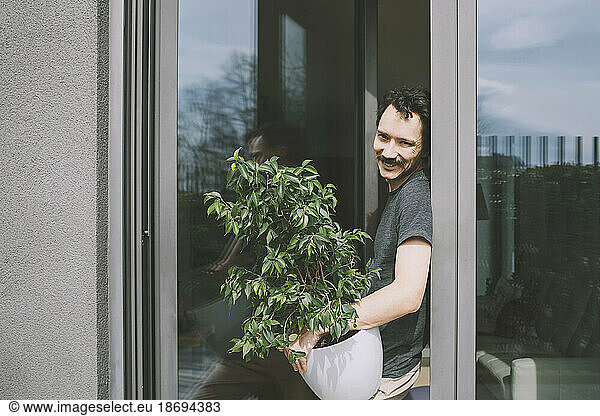 Happy man standing with potted plant by glass door