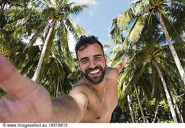 Happy man taking selfie with tropical tress in background