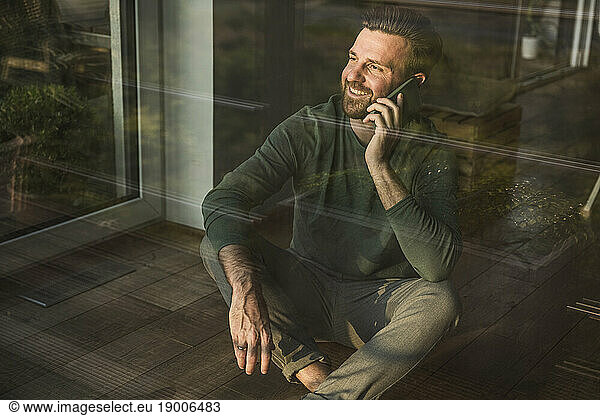 Happy man talking on smart phone sitting at home
