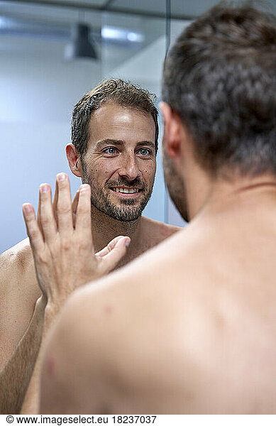 Happy man touching and looking in mirror at home