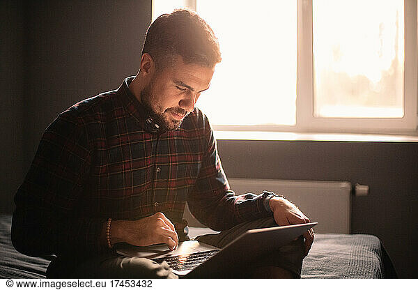 Happy man using laptop computer sitting on bed at home