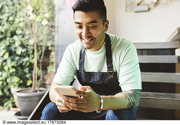 Happy man using mobile phone sitting on steps in coffee shop