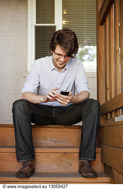 Happy man using phone while sitting on steps