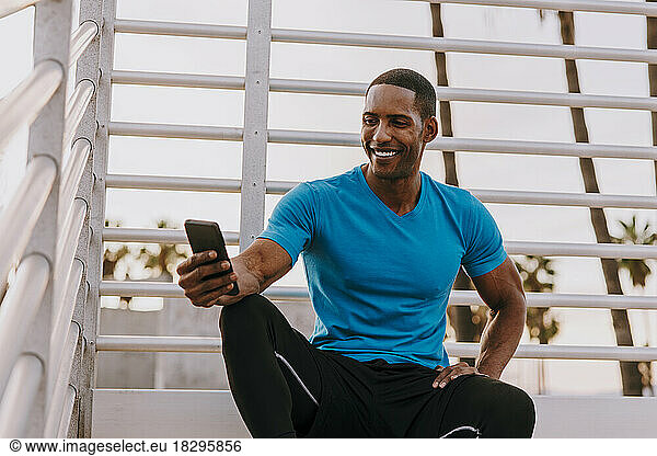 Happy man using smart phone sitting in front of railing