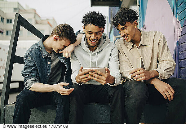 Happy man using smart phone while sitting with friends outdoors