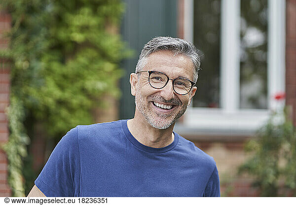 Happy man wearing eyeglasses in front of house