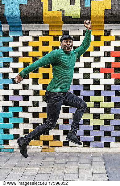 Happy man wearing flat cap jumping in front of multi colored wall