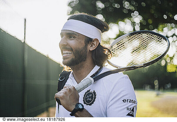 Happy man wearing headband looking away holding tennis racket