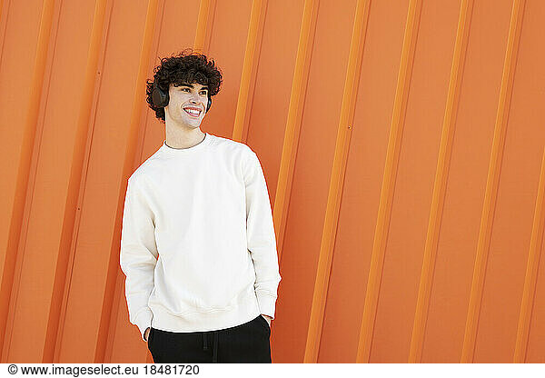 Happy man wearing headphones in front of orange wall
