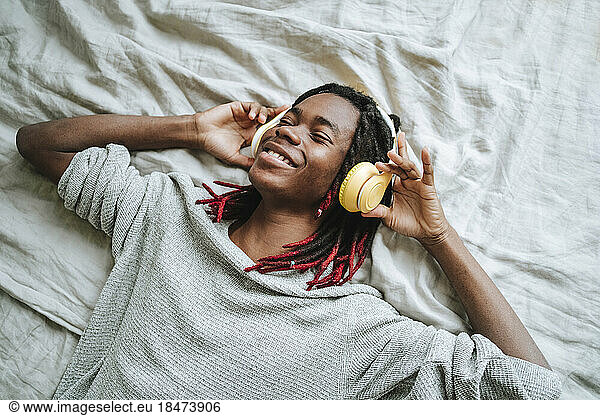 Happy man wearing headphones listening to music lying on bed at home