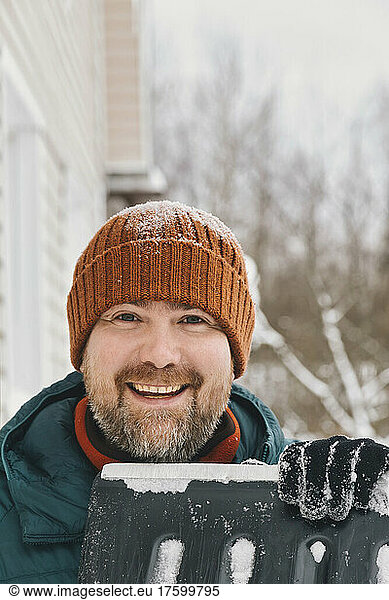 Happy man wearing knit hat holding snow shovel in winter