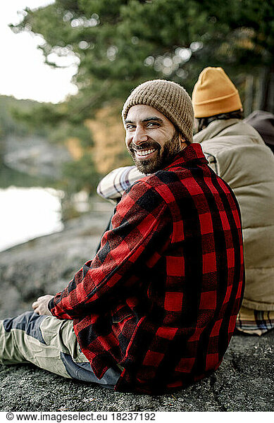 Happy man wearing plaid shirt looking over shoulder while sitting on rock