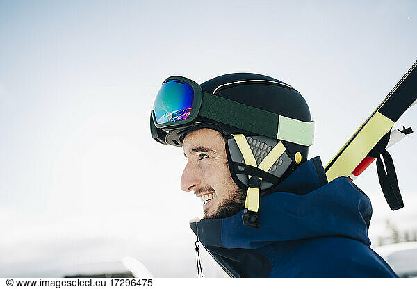 Happy man wearing ski goggles and helmet while looking away against sky