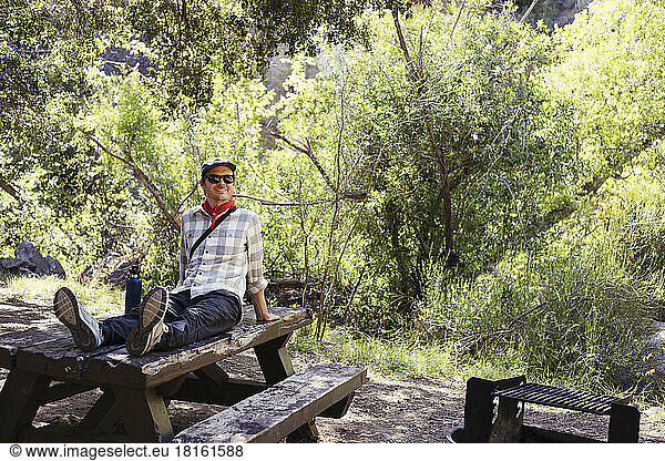 Happy man wearing sunglasses on wooden table in forest