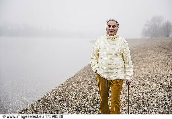 Happy man wearing warm clothing walking with hand in pocket at beach