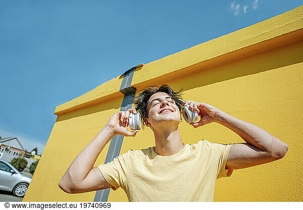 Happy man wearing wireless headphones enjoying music in front of yellow wall