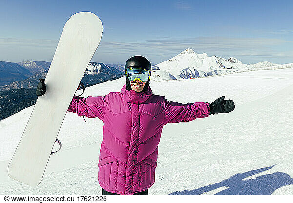 Happy man with arms outstretched holding snowboard on snowy mountain