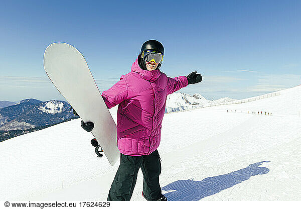 Happy man with arms outstretched holding snowboard on sunny day
