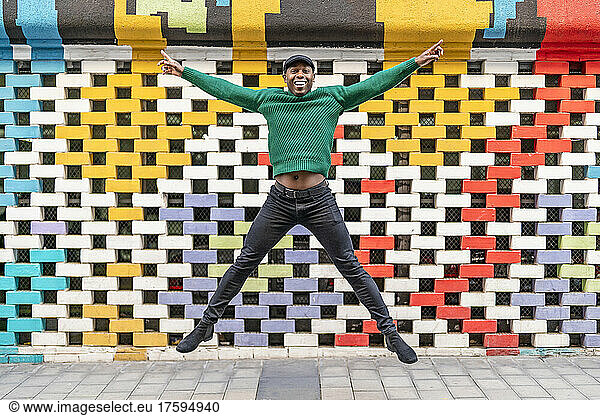 Happy man with arms outstretched jumping in front of multi colored wall
