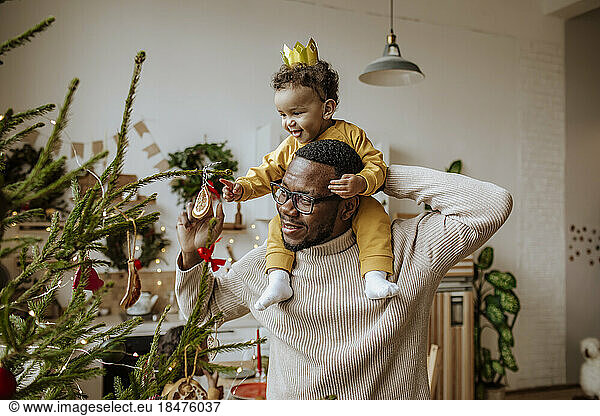 Happy man with daughter touching Christmas ornaments at home