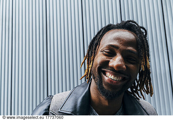 Happy man with dreadlocks in front of wall