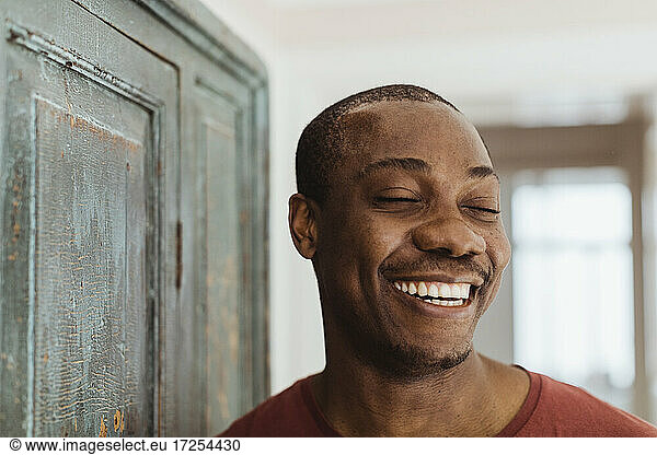 Happy man with eye closed by closet at home