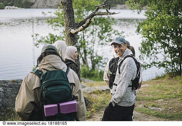 Happy man with hand in pocket during hiking with friends in forest