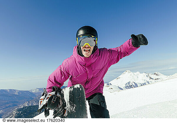 Happy man with hand raised enjoying at ski resort on sunny day