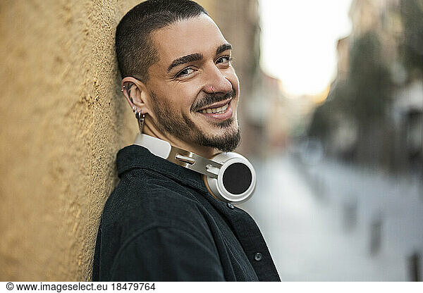 Happy man with headphones leaning by wall