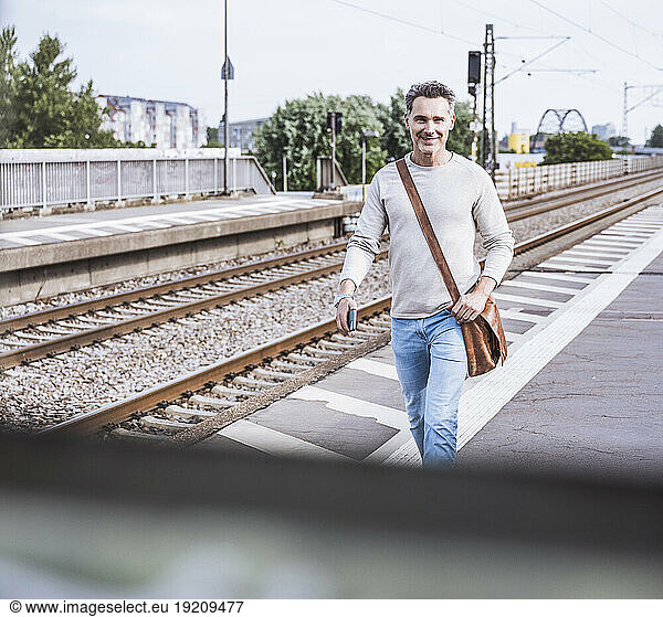 Happy man with shoulder bag walking at railroad station