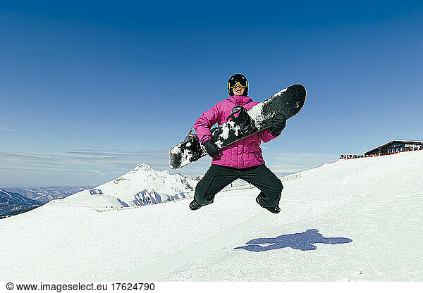 Happy man with snowboard jumping on snow in winter