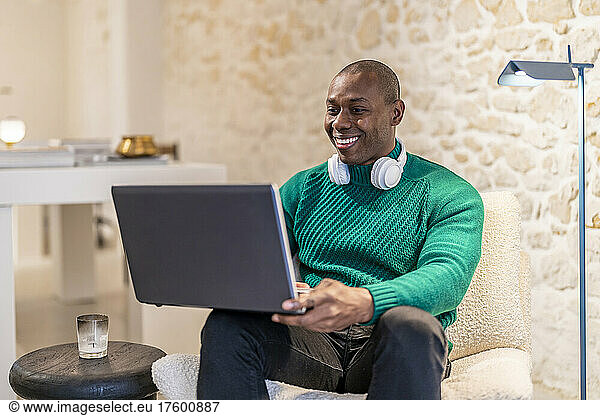 Happy man with wireless headphones using laptop working at home