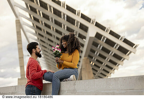 Happy man with woman holding bouquet of flowers in front of solar panels