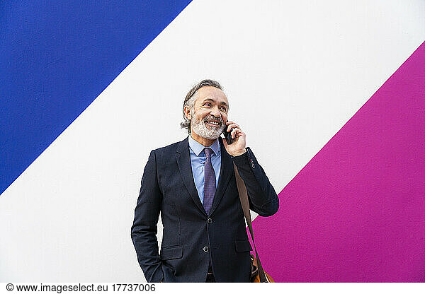 Happy mature businessman talking on mobile phone in front of multi colored wall