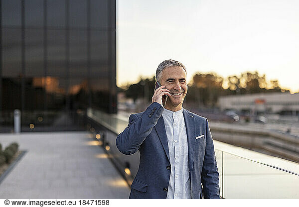 Happy mature businessman talking on smart phone at office park
