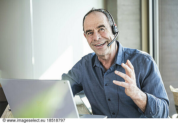 Happy mature businessman wearing headset discussing over laptop in office