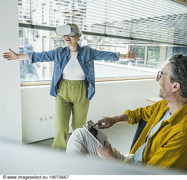 Happy mature businessman with colleague wearing virtual reality simulators in office