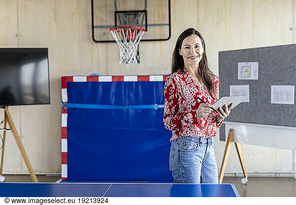 Happy mature businesswoman standing with tablet PC in modern office