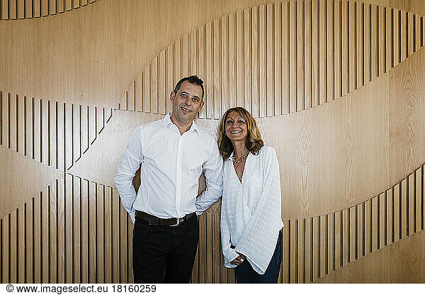 Happy mature businesswoman with colleague standing in front of wooden wall