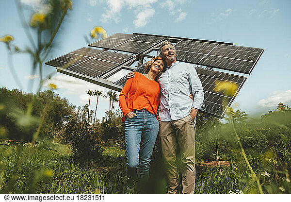 Happy mature couple embracing each other in front of solar panels